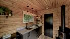 A photo showing the cedar-clad cabin interior, kitchen area and woodburner