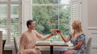 Two women sitting at a table by a window clinking their cocktail glasses together