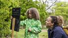 A child and parent looking at a trail sign in a garden.