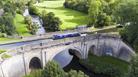 blue narrowboat floats across aqueduct over green valley