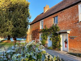 Jane Austen's House in winter.  Frost is on the ground and a red wreath decorates the door.