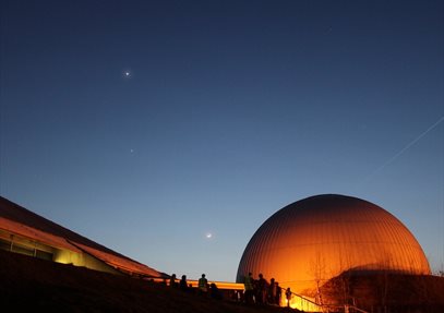 A dark sky with a few stars. The Science Centre and Planetarium are glowing orange against the night sky.