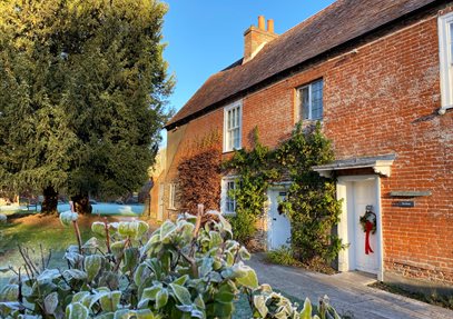 Jane Austen's House in winter.  Frost is on the ground and a red wreath decorates the door.