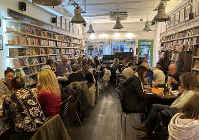 Groups of people sitting at tables in a bookshop with drinks taking part in a quiz