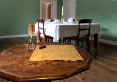 Jane Austen's small wooden writing table. A quill and letter sit on the table.