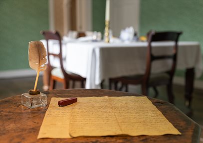 Jane Austen's small wooden writing table. A quill and letter sit on the table.