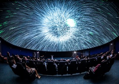 A blast of white light on a Planetarium dome. There are people sat in seats watching the screen.