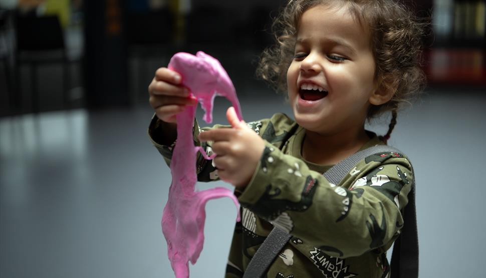 A young girl holding pink slime. The girl is looking at the slime with a big smile on her face.