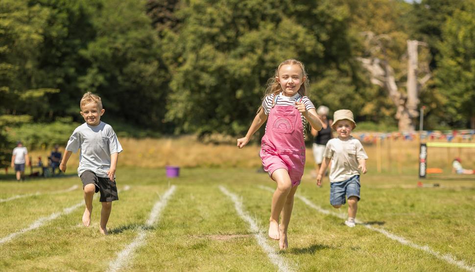 Children run a relay race on a sunny lawn.