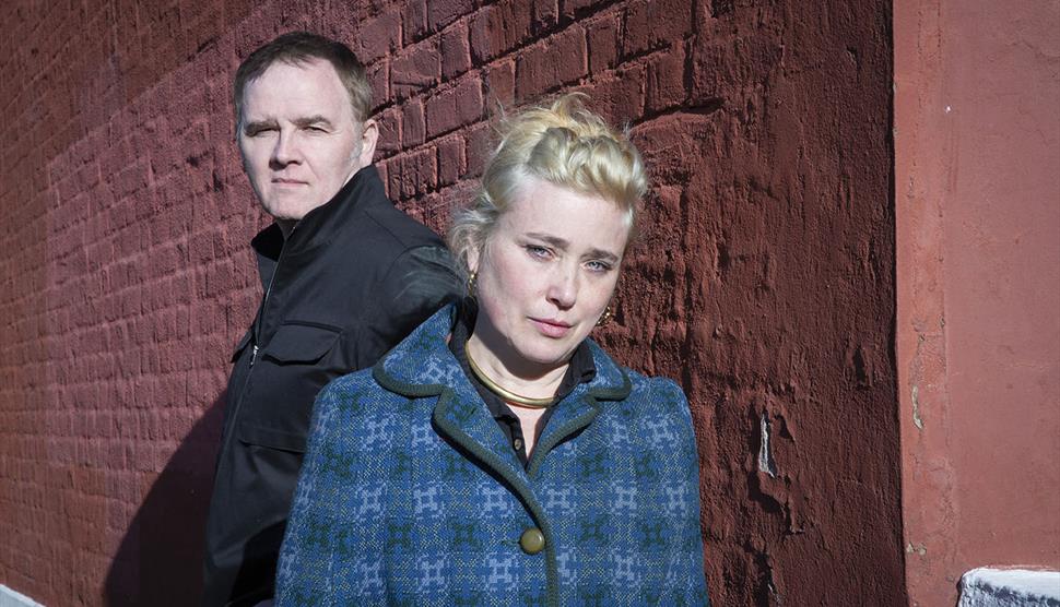 A man and a blonde woman stand together in front of a building.