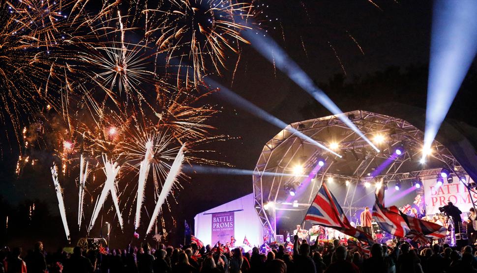 A large crowd waving flags in front of an open air stage and fireworks