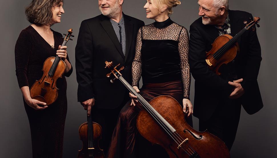 A group of musicians holding string instruments smile at each other.