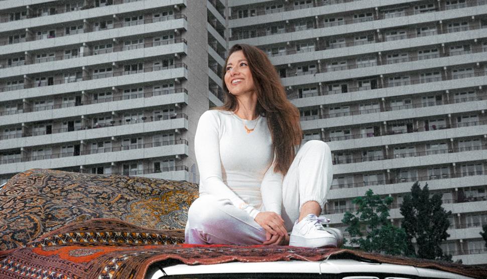 Yazz Ahmed sits on top of a car with a decorative carpet underneath her.