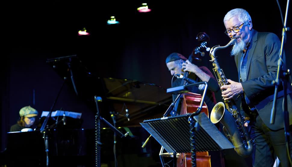 A saxophonist, double bassist and pianist perform on stage.