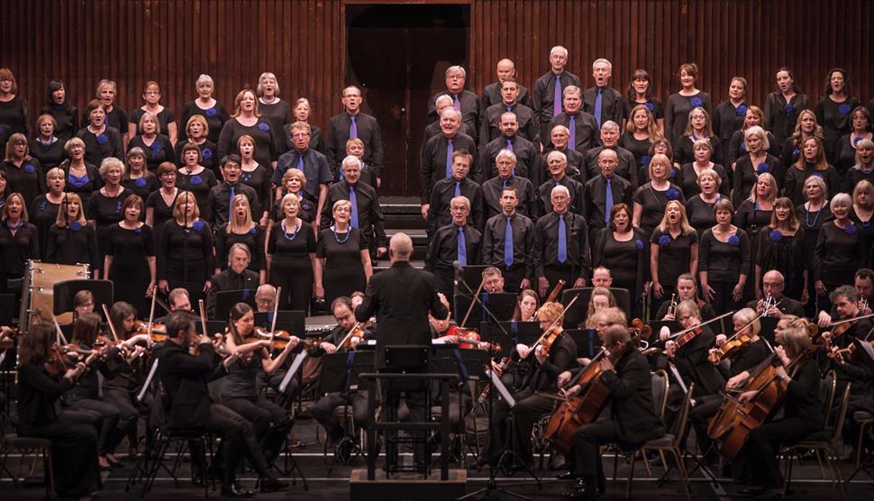 On the stage at the O2 Southampton, the choir stand on the choir steps as the orchestra perform on the stage, with the conductor standing in front of