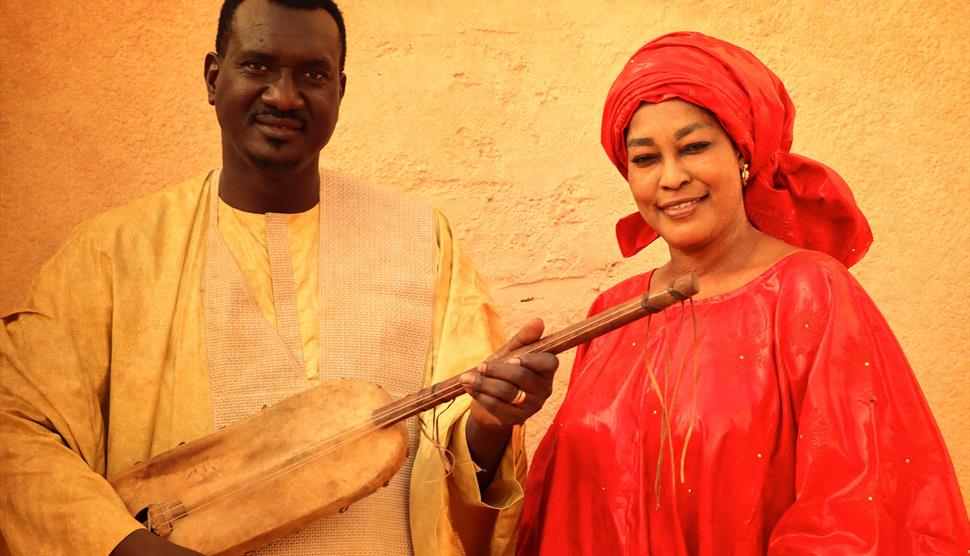 A man wearing white and a woman wearing red stand together.