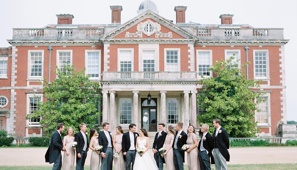 A bride and groom stand outside Stansted Park accompanied by the bridal party.
