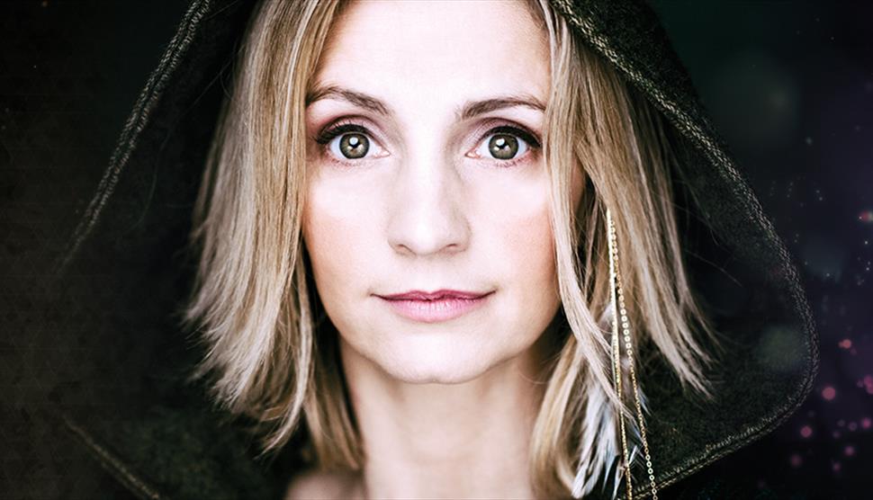 A blonde woman wearing a black hood looks towards the camera.