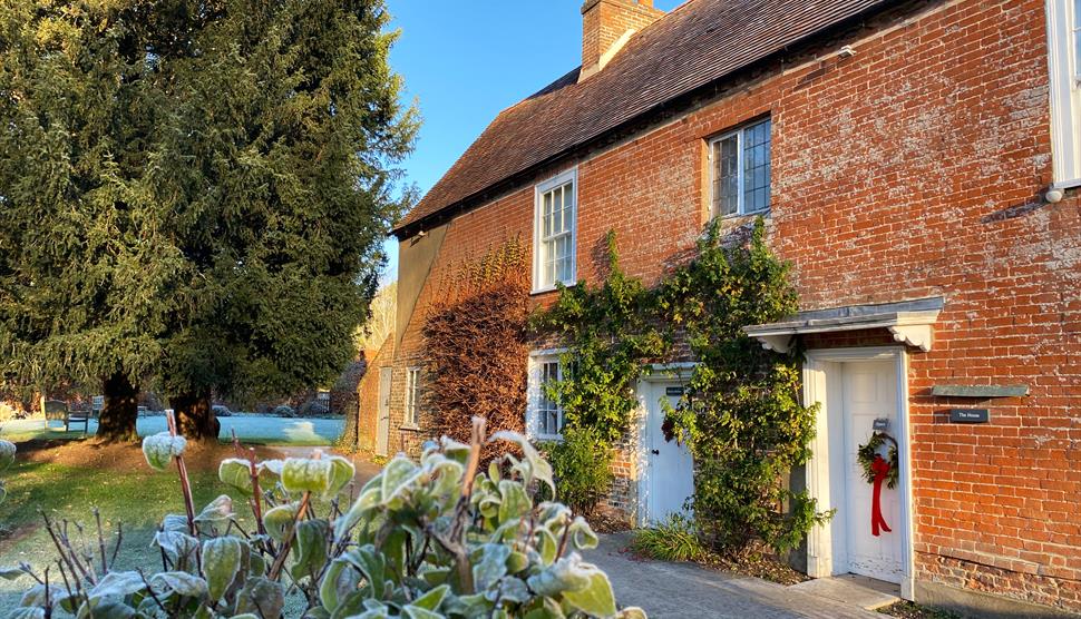 Jane Austen's House in winter.  Frost is on the ground and a red wreath decorates the door.