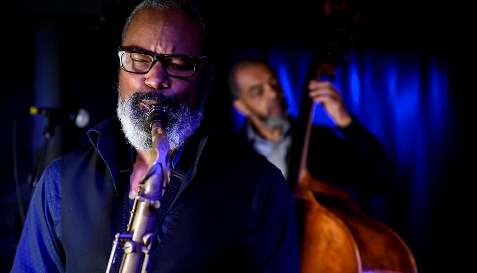Denys Baptiste is in the front of the shot playing the tenor saxophone, and Gary Crosby OBE is playing acoustic bass behind him.