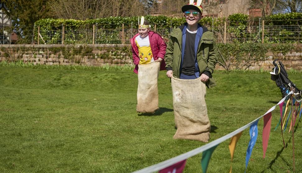 Two children wearing bunny ears, having a sack race.