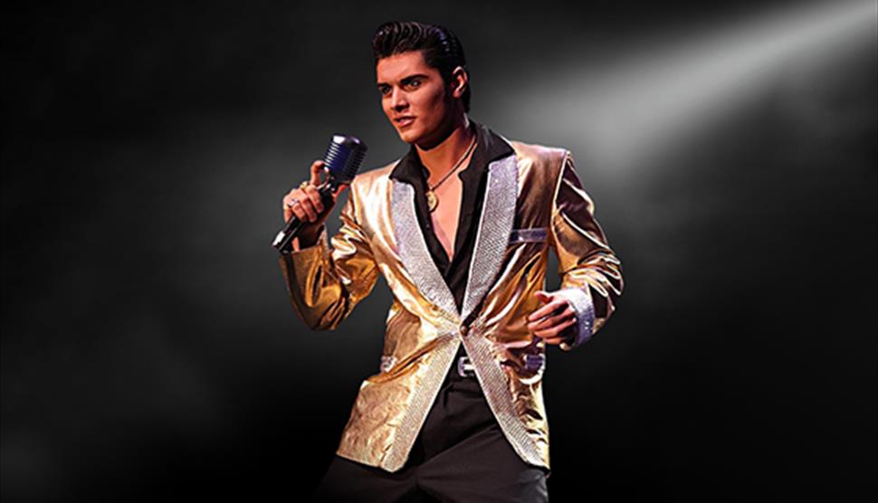 Emilio Santoro dressed as Elvis in a shiny gold suit jacket, holding a microphone on a dark background