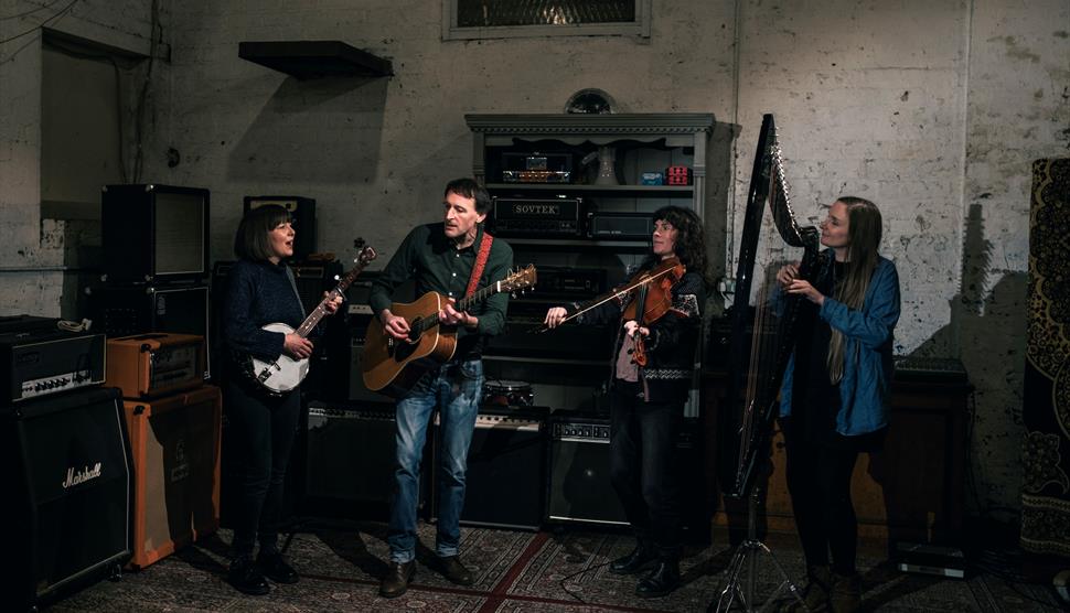 A band made up of a woman playing a banjo, a man playing guitar, a man playing the fiddle and a woman playing the harp.