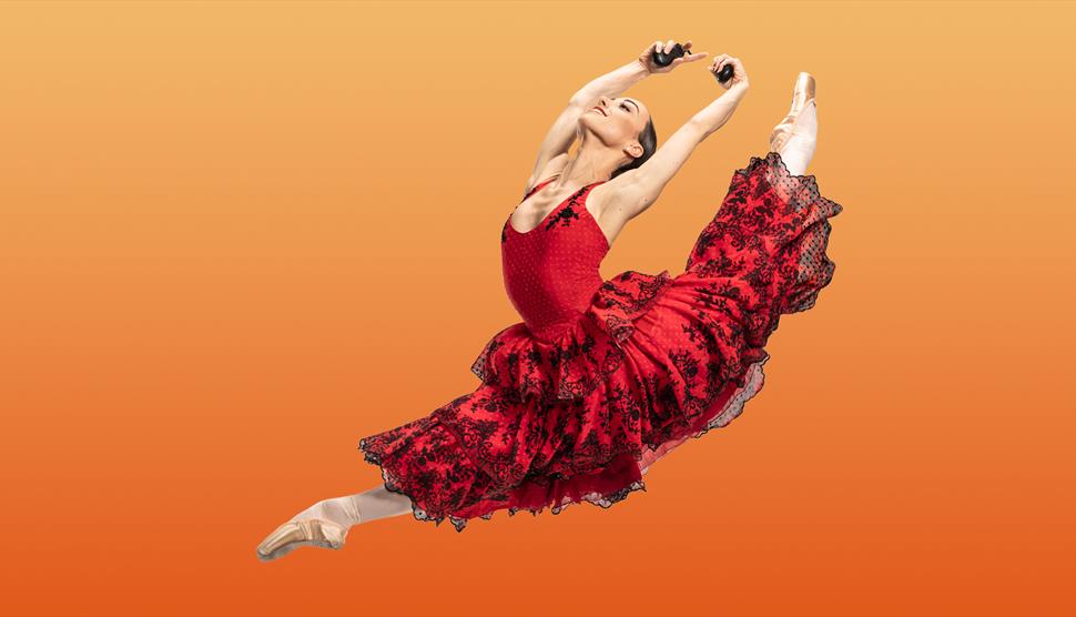 Ballet dancer in red dress leaps through air. Orange background.