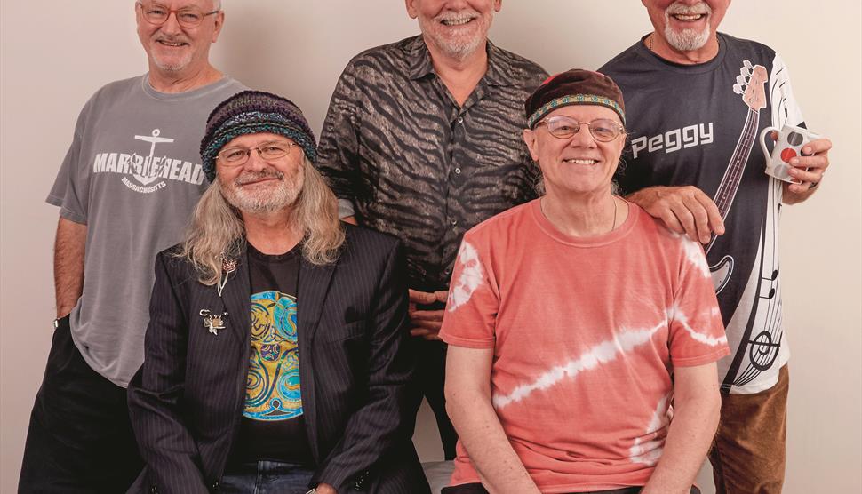 Five musicians sing and play their instruments, including fiddles and guitars.