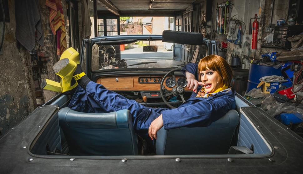 Natalie Spanner sits in a classic car with her feet up, wearing yellow platform shoes and a boiler suit