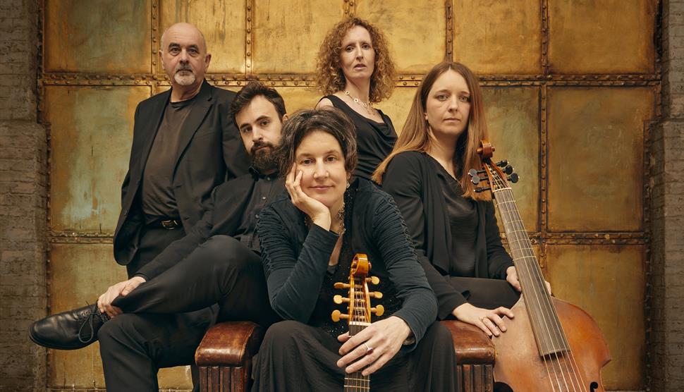 Five men and women sit on a wooden stool facing the camera. Two of them are holding viols.