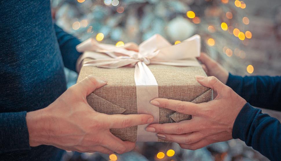 A wrapped gift is being passed from one pair of hands to another