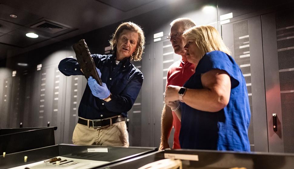 A member of the Mary Rose Museum team showing an artefact to a man and woman.