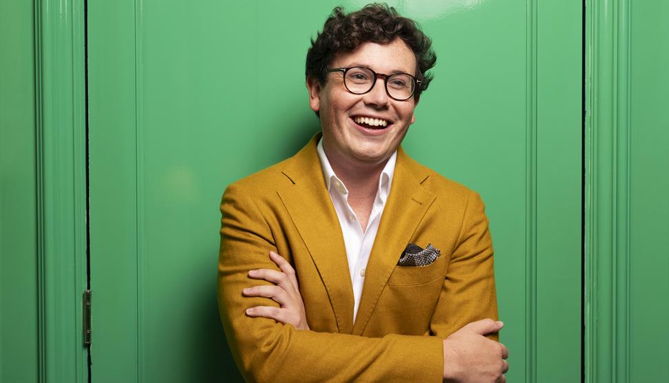 Pianist Martin James Bartlett is stood smiling in front of a green background
