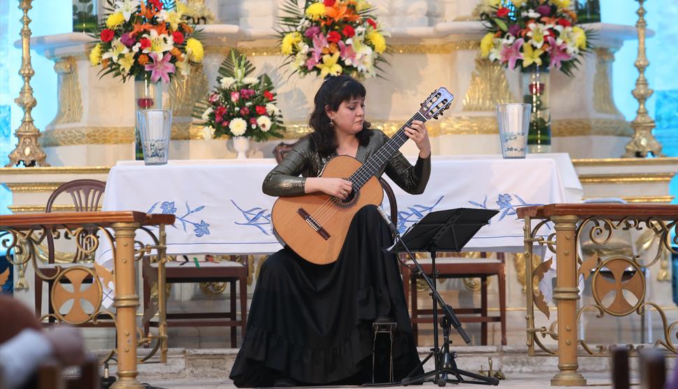 A woman with black hair plays the guitar in a cathedral.