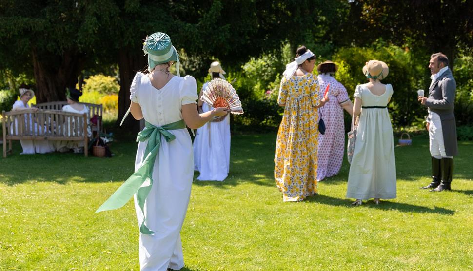 Visitors in Regency dress walking across the cottage garden at Jane Austen's House in summer