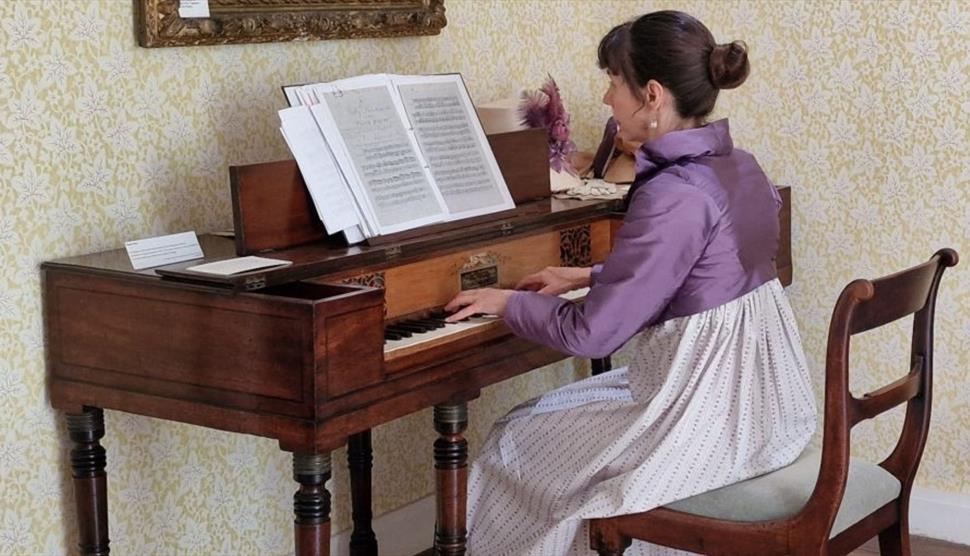 A woman in regency clothing playing on a piano