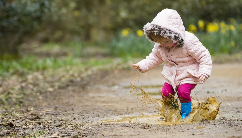 A young child jumps in a muddy puddle.