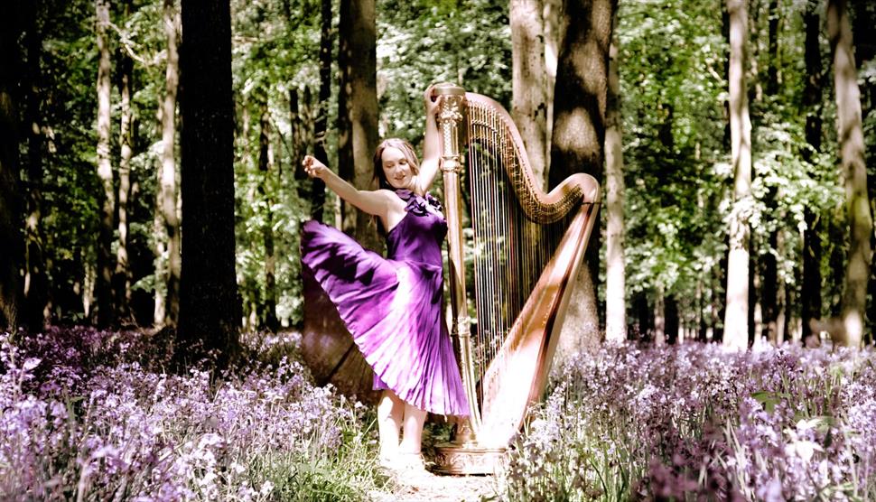 Keziah Thomas playing her harp in a beautiful, flowering spring wood.