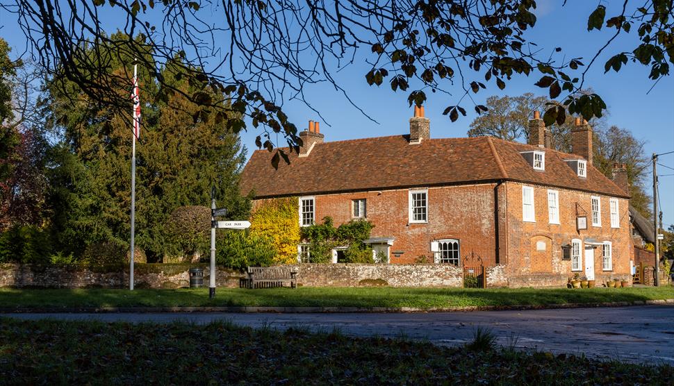 Jane Austen's House from the garden in Autumn.  Brown and orange leaves carpet the ground.