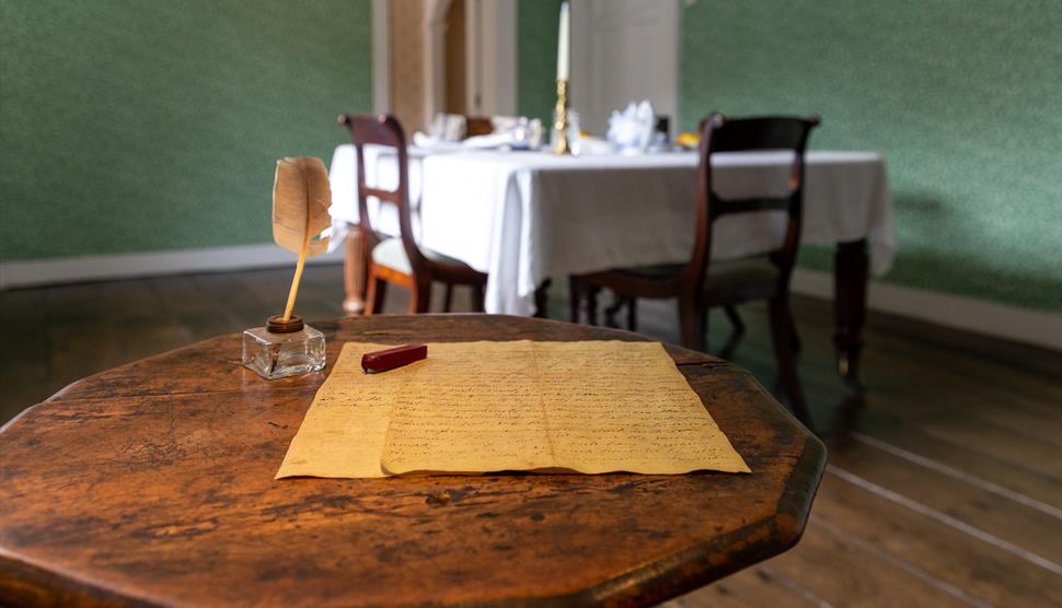 Jane Austen's small wooden writing table. A quill and letter sit on the table.