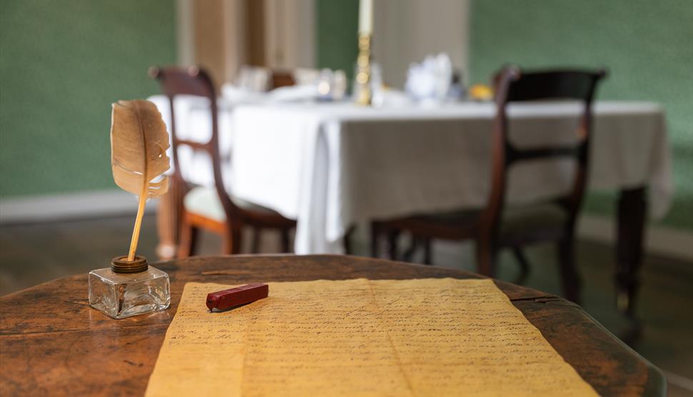Jane Austen's small wooden writing table. A quill and letter sit on the table.