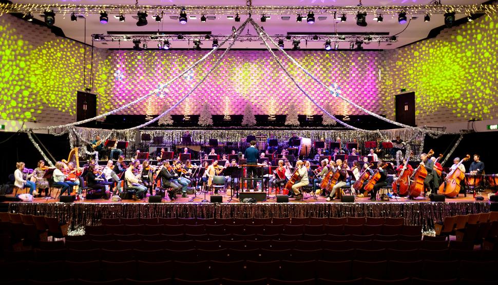 The orchestra are performing onstage surrounded by festive decorations