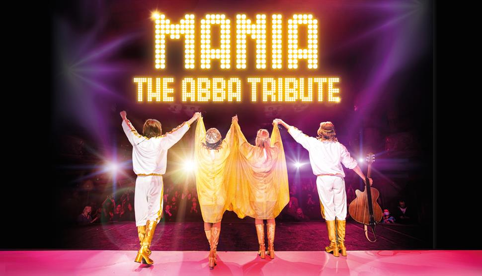 Four performers in ABBA costumes stand on stage facing the audience