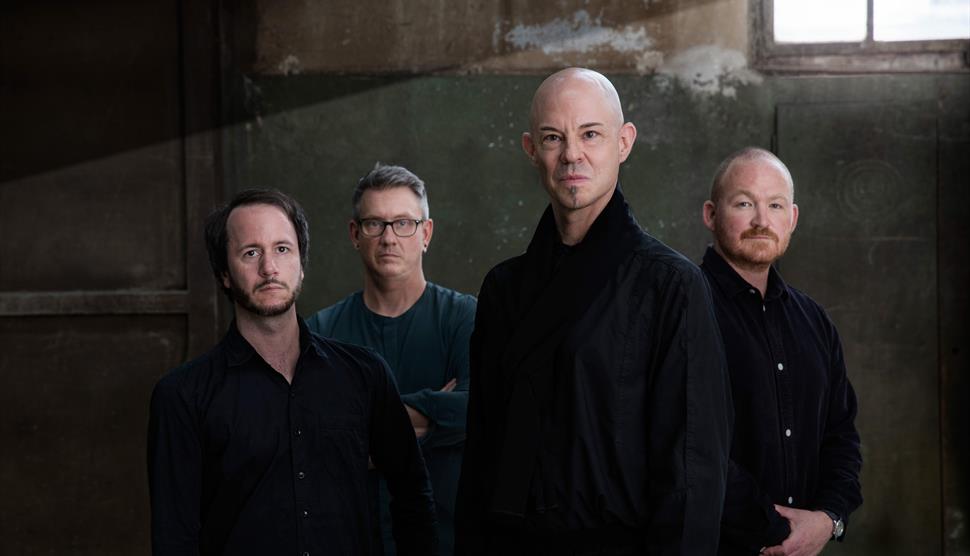 Four men stand in a room together.