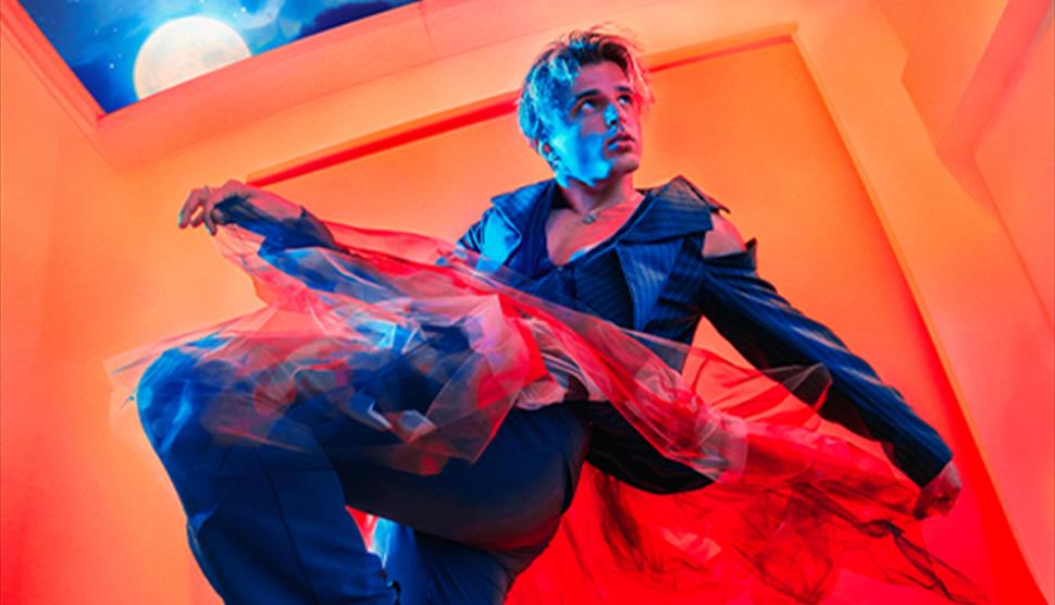Nikita Kuzmin is dressed in a stylish outfit, blending modern and theatrical elements, with flowing, translucent fabric, adding a sense of movement. T