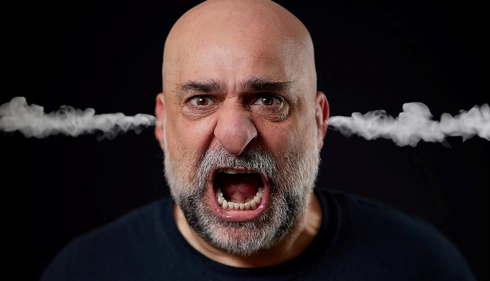 A photographic portrait of a bald man with a grey beard - Omid Djalili - screaming, with steam coming out of his ears