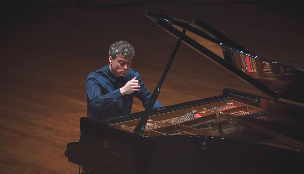 A man with grey, curly hair plays the piano on stage.