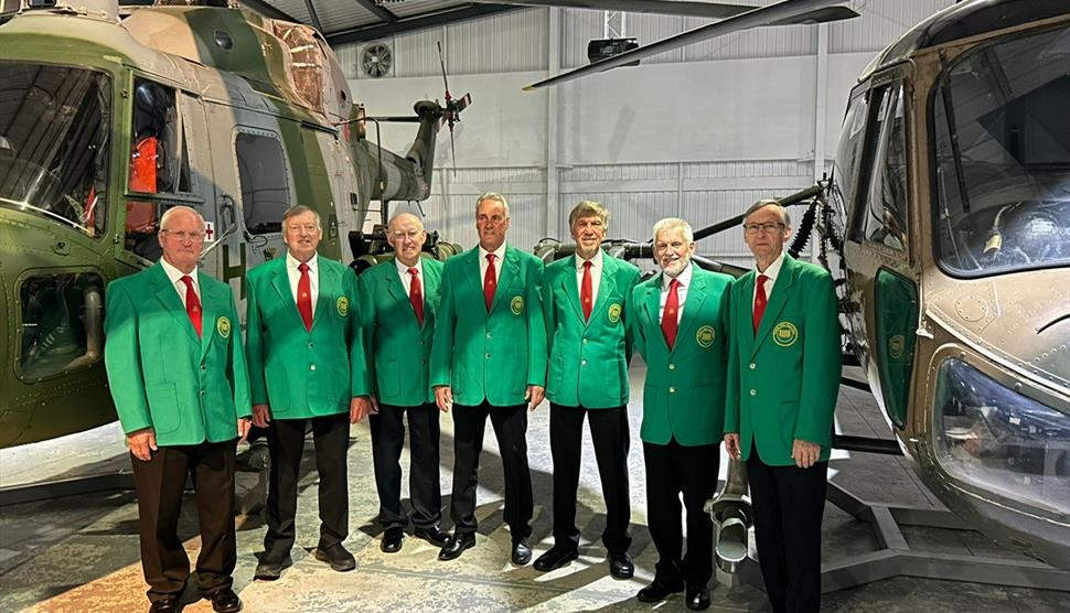 Image of the Romsey Male Voice choir in front of helicopters at the Army Flying Museum