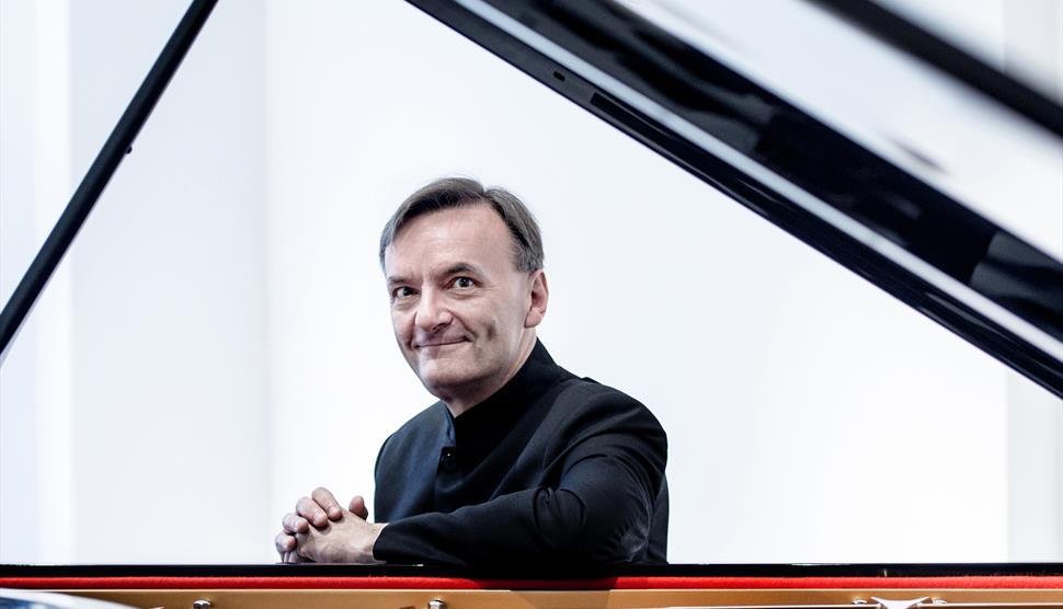 A man sits at a piano and looks towards the camera.